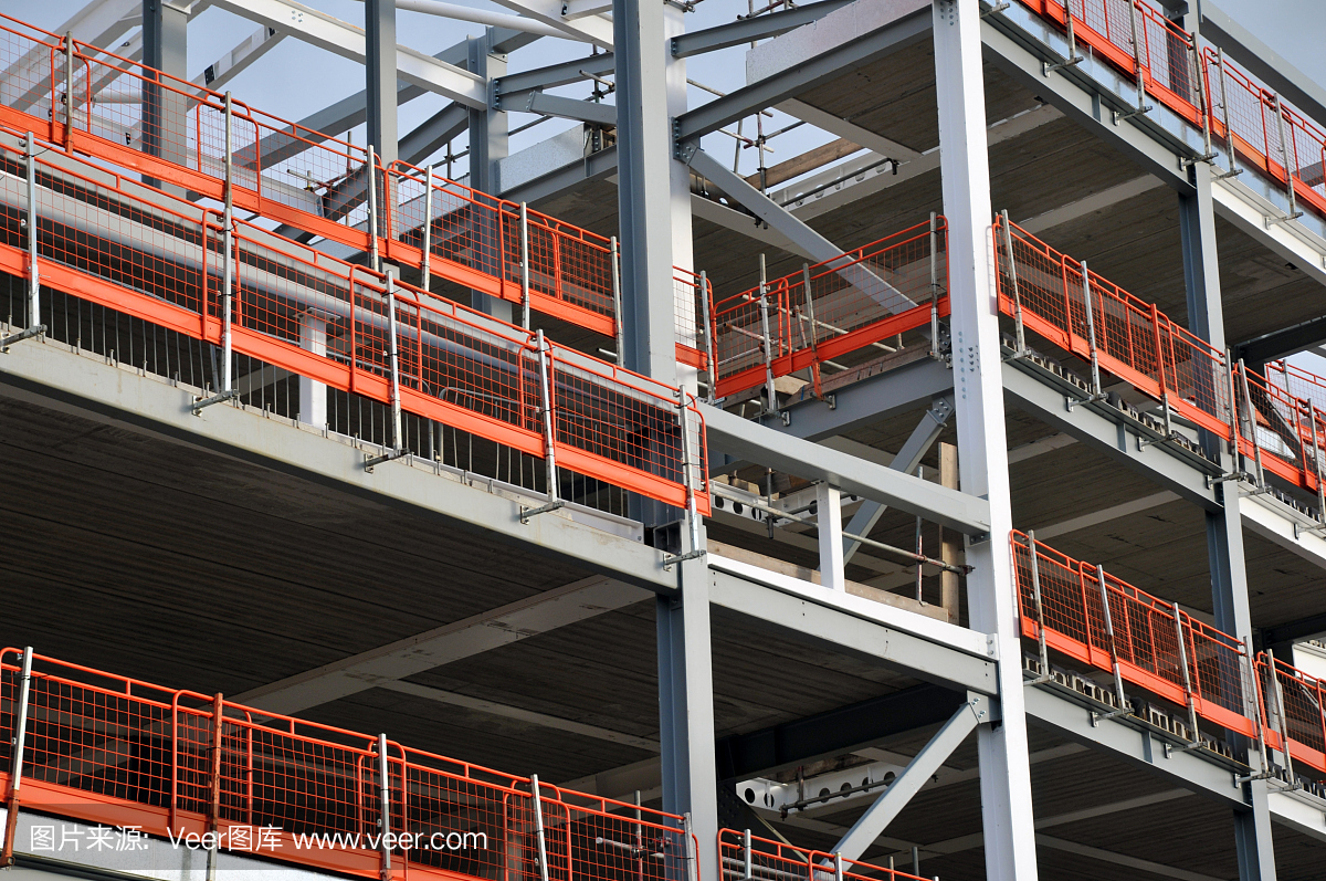 在蓝色天空的映衬下,一座正在施工的钢架建筑,有大梁和橙色的安全栏杆